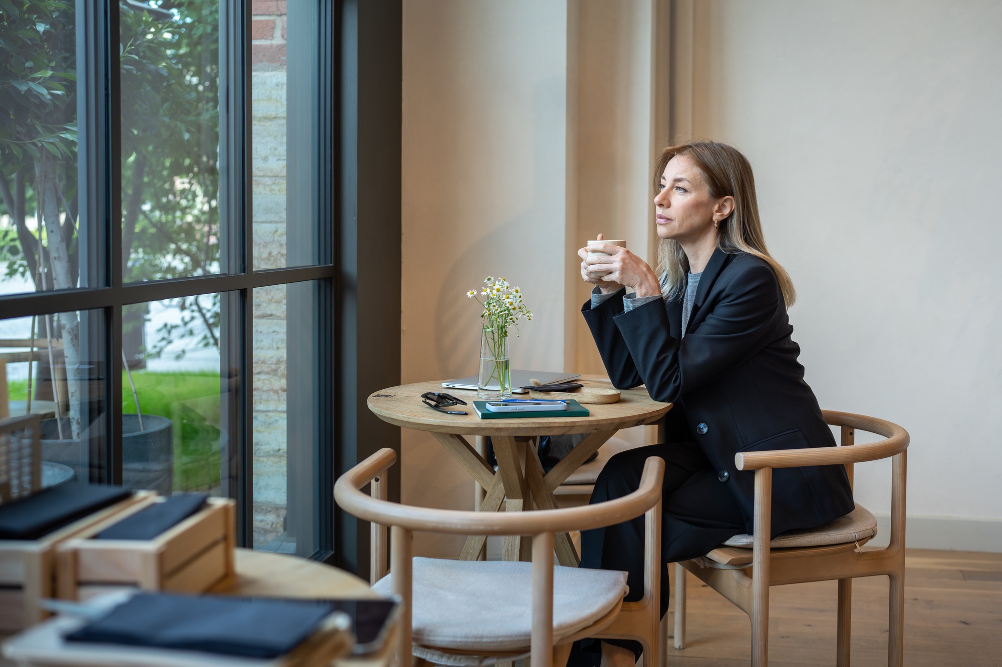 Tired, thoughtful businesswoman on coffee break in cafe with laptop and smartphone, battling burnout